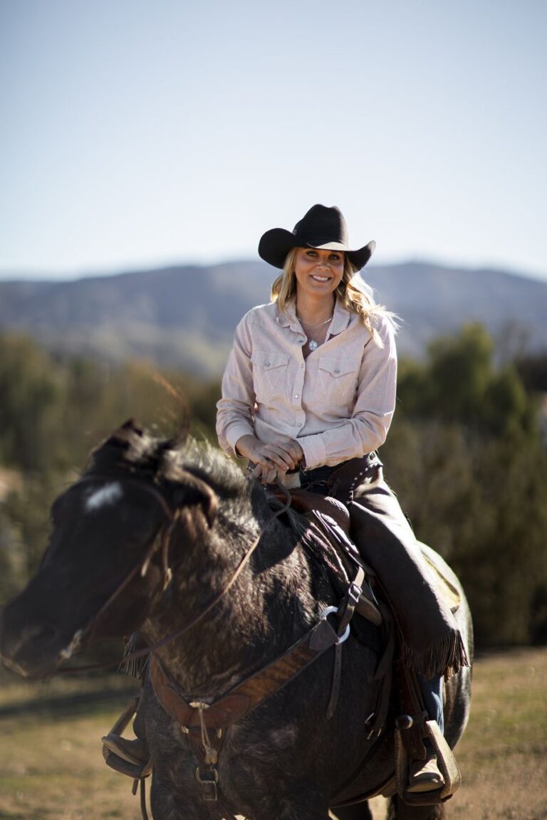 A picture of Equine Emma sitting on a horse with hills in the background.